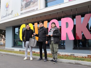 Drei Männer stehen vor einem bunten Schriftzug